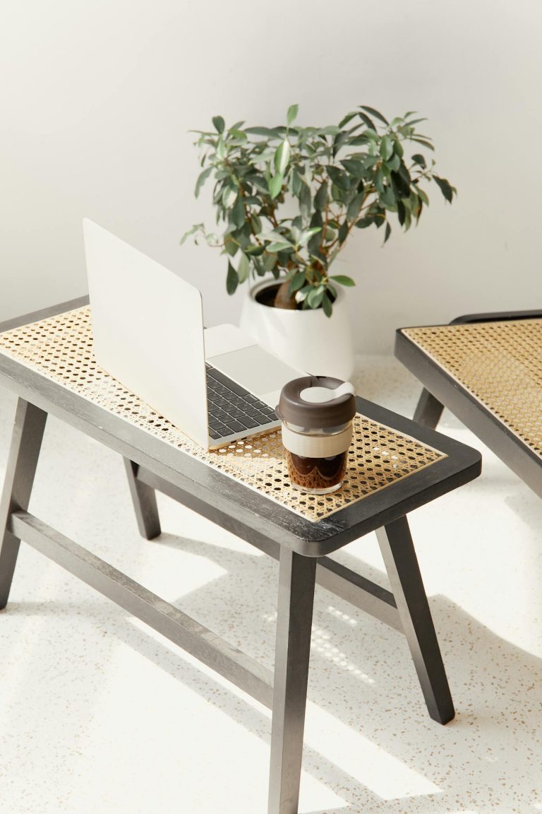 A sleek minimalist setting featuring a laptop and reusable coffee cup on a woven bench.
